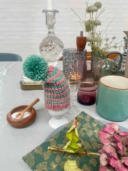 Æggevarmer ska Nissehue i lyserød og turkis strik med pom pom.